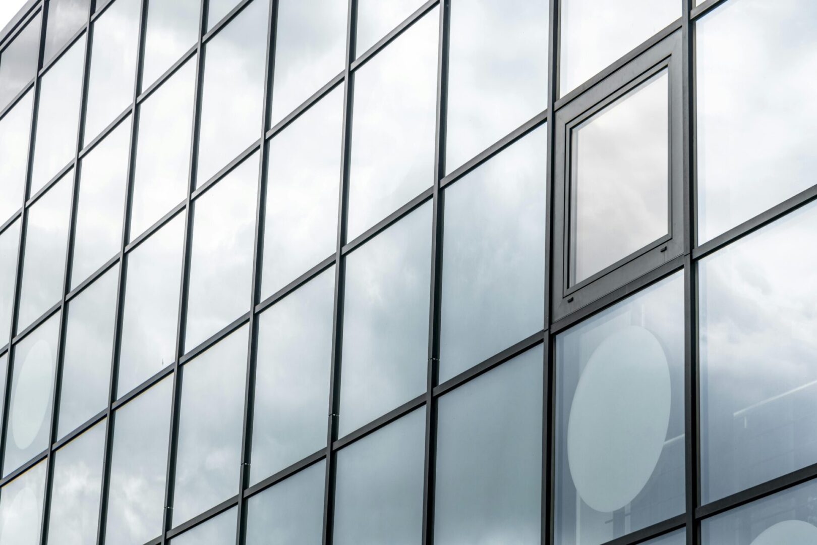 A window in the side of a building with clouds reflected on it.